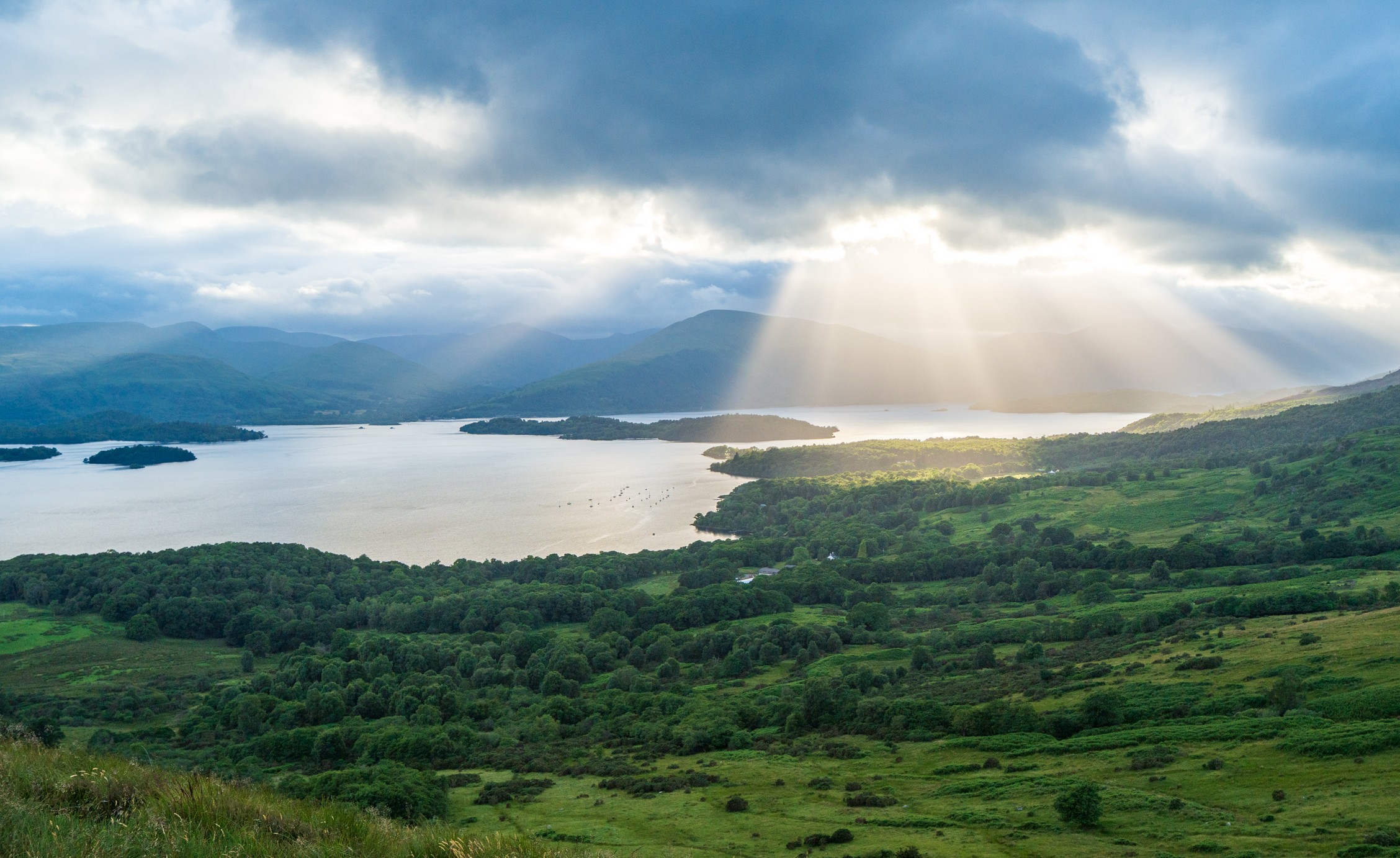 Loch Lomond from high up with green foregrouns and a sunburst top right