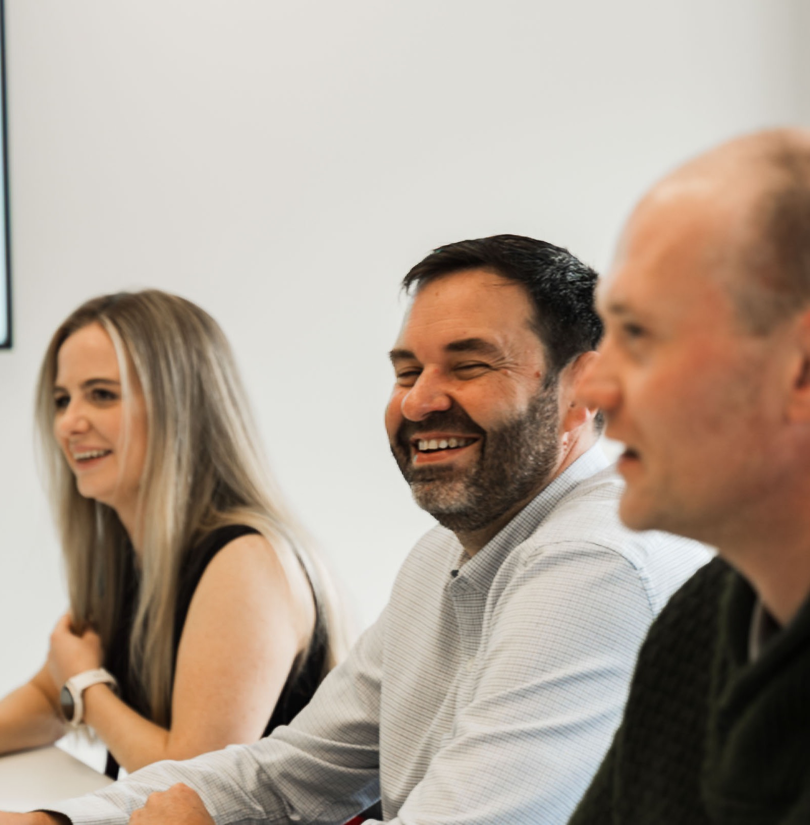 Tight in on woman and two men sitting side by side in a meeting room