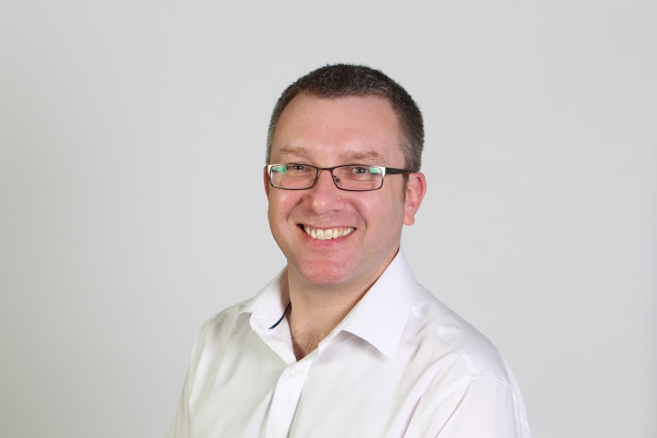 Headshot of Alex Lungley in a white shirt with no tie, smiling