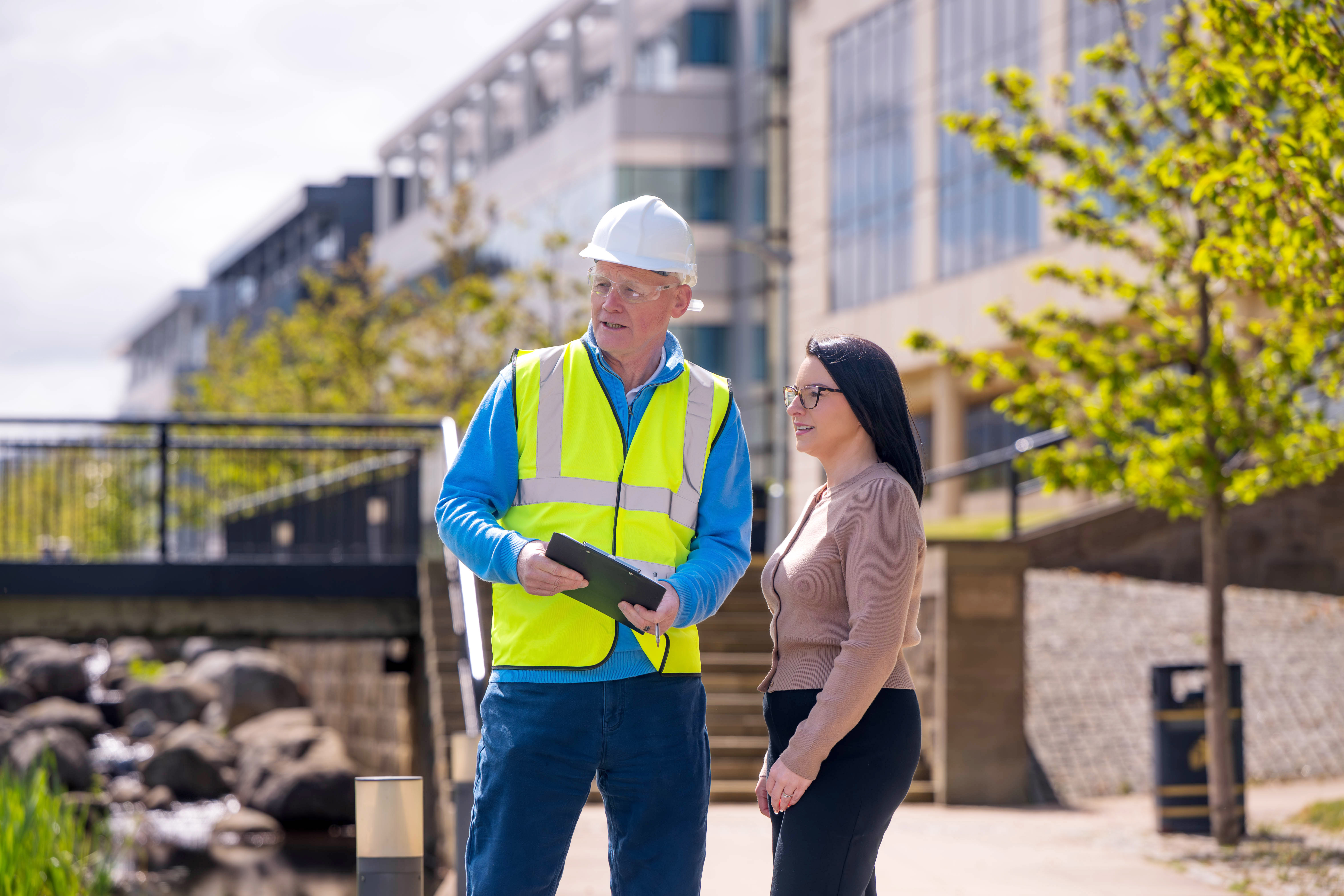 A construction worker and a woman in plain clothes surveying something off camera