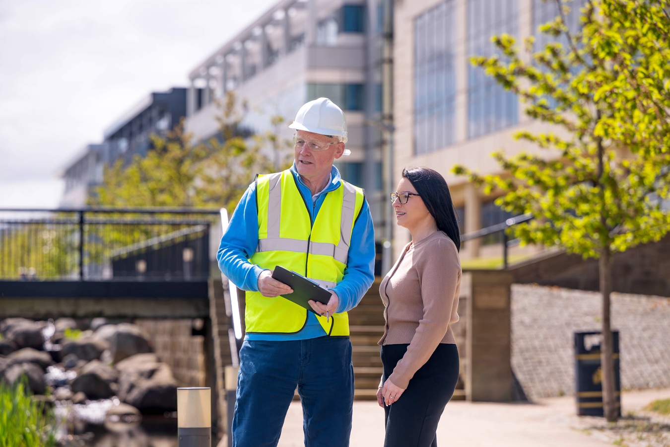 A construction worker and a woman in plain clothes surveying something off camera