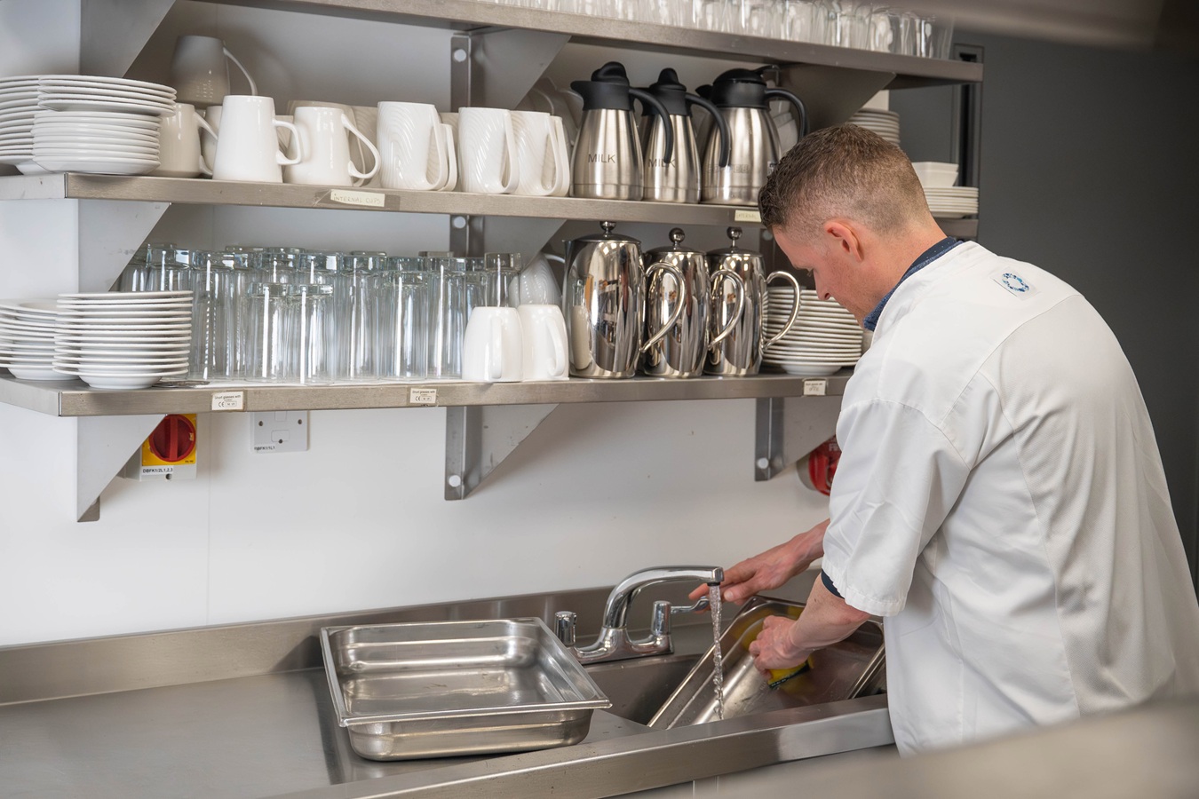 A man in kitchen whites, washing up in a commercial kitchen
