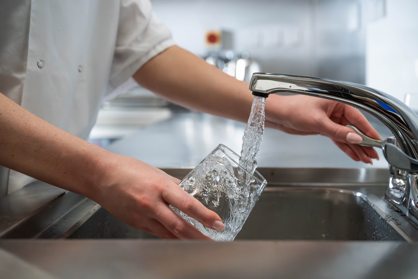 A man filling a glass with water from a metallic sink