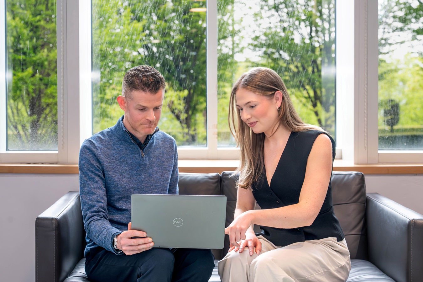 Two people chatting, in a business setting, on a sofa and with a laptop