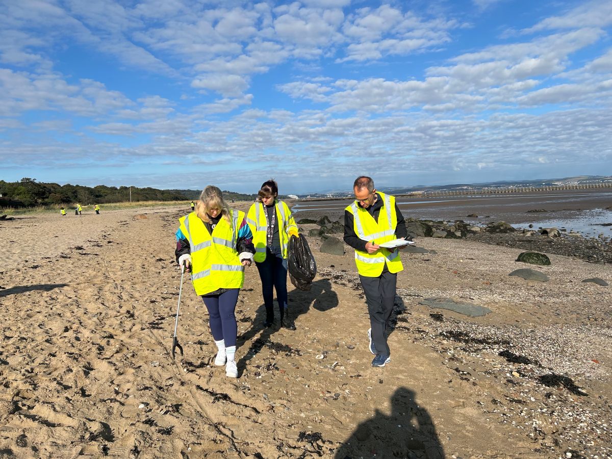 Three Business Stream colleagues in hi-vis vests picking up litter on a beach