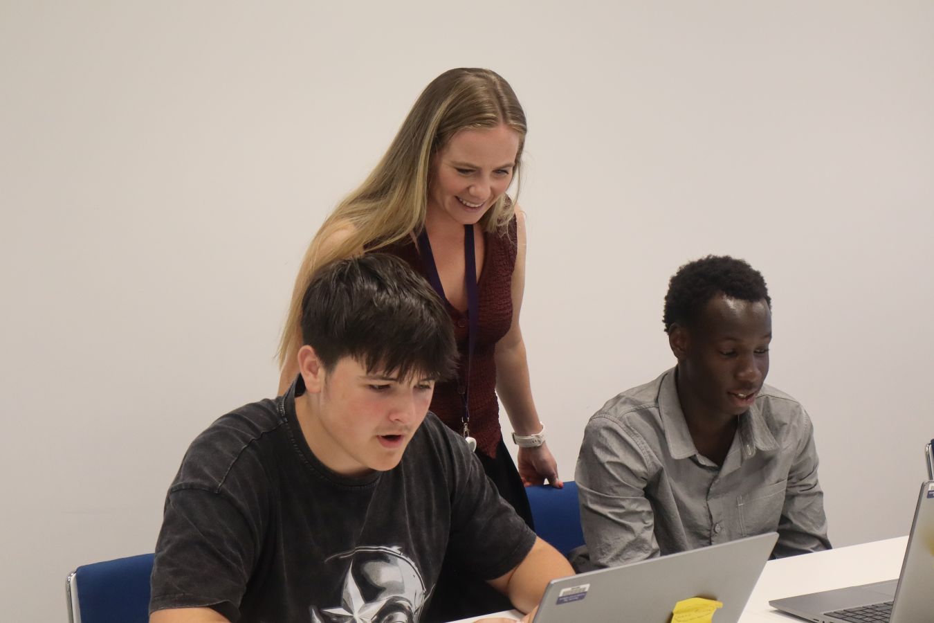 Woman standing and two young men seated looking at laptop