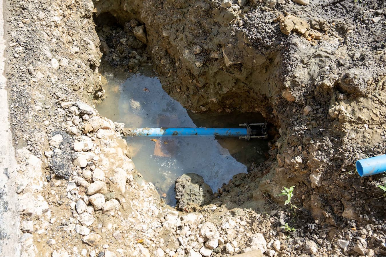 Hole in ground showing leaking external water pipe in pool of water
