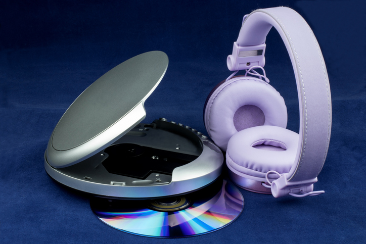 Lilac headphones next to a portable CD player and an audio CD