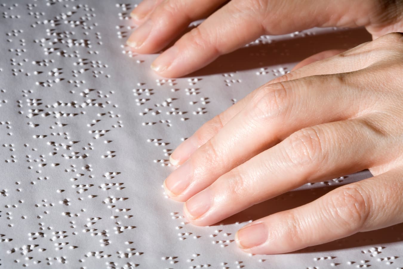Hands right of shot reading braille text on white paper