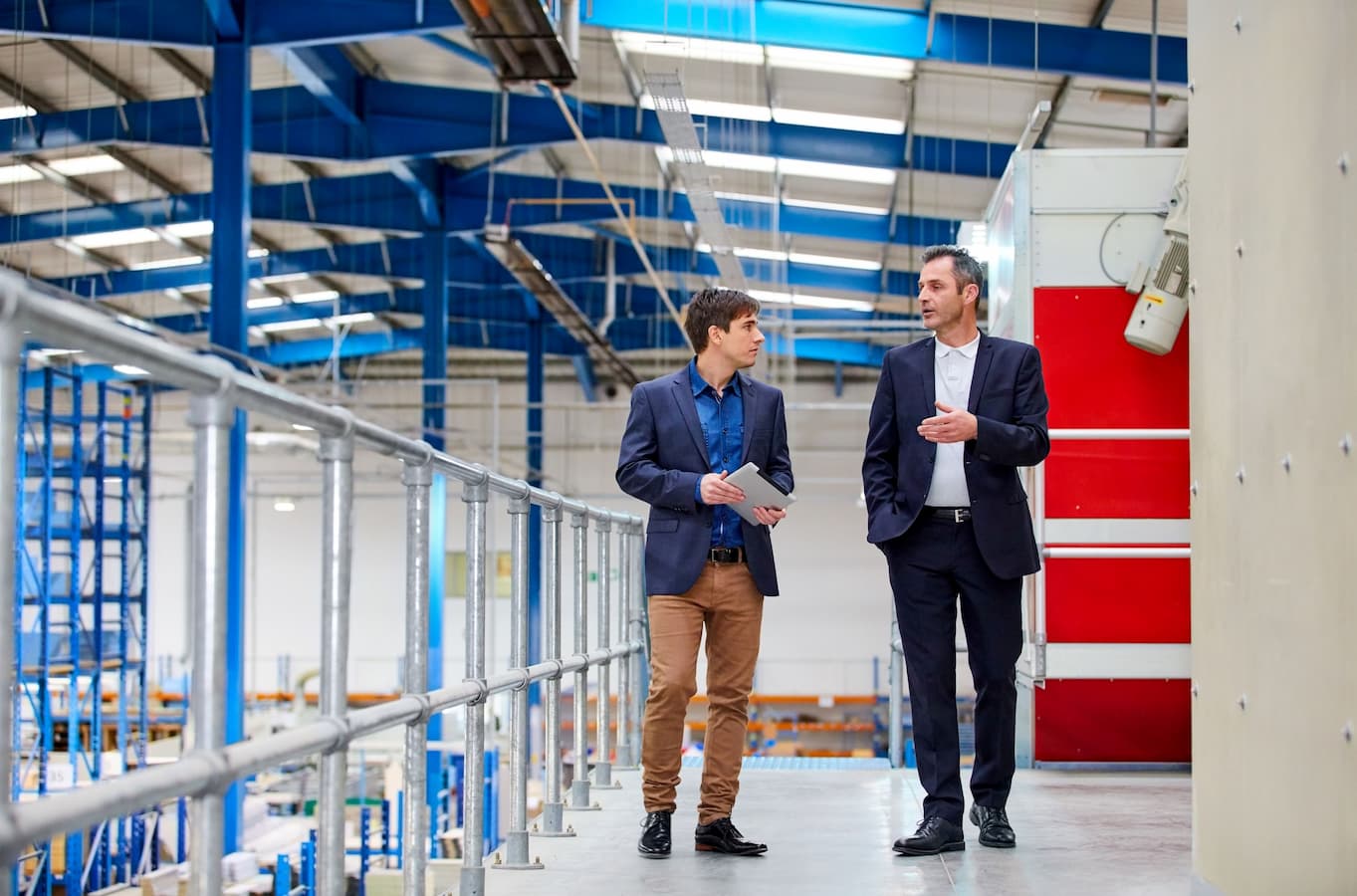 Two smartly dressed men talking as they walk through a large factory setting