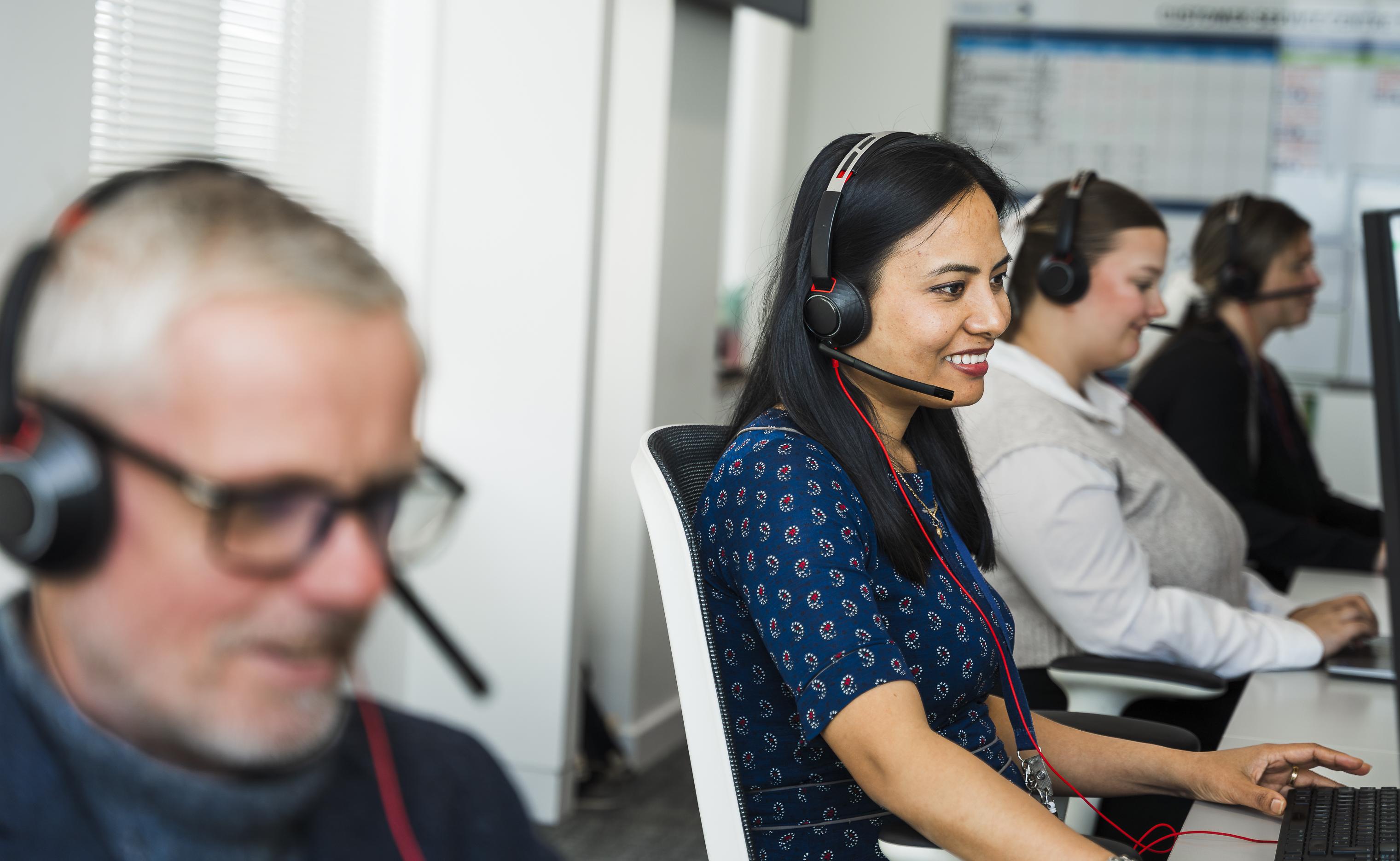 Three women and a man wearing headsets and smiling in a customer service setting