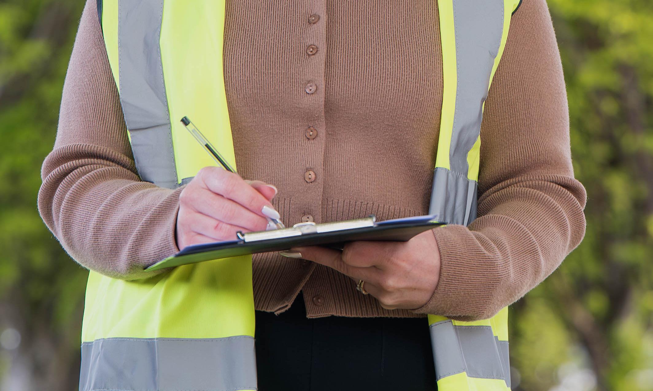 Close-up of woman in hi-vis vest writing on a clipboard