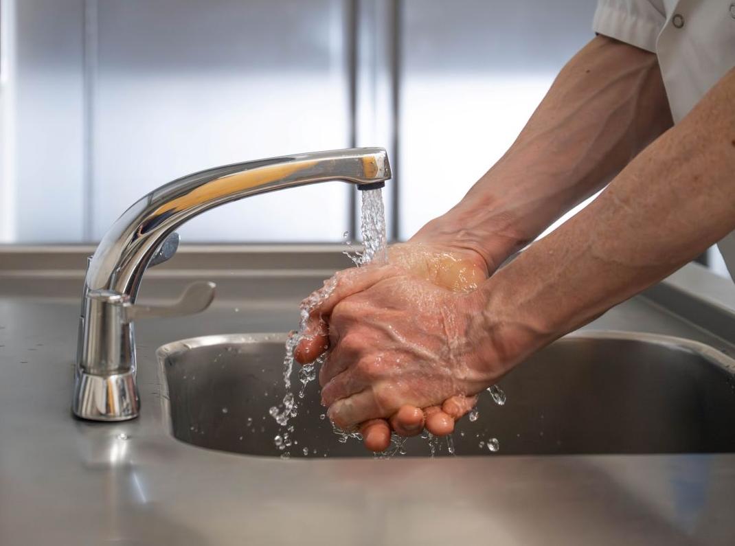 Man washing hands under running tap in commercial kitchen