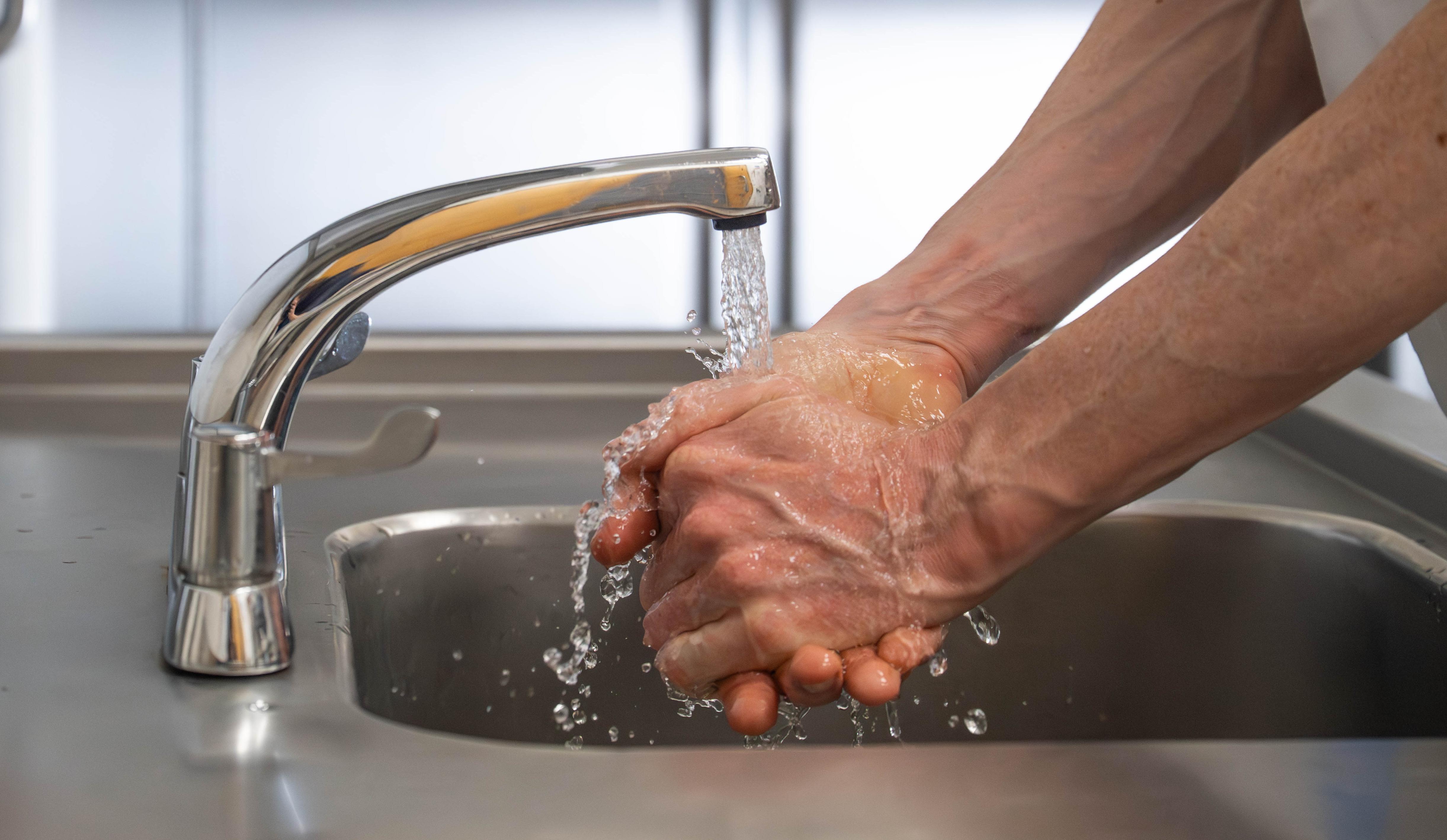 Close-up of man washing hands under running tap in commercial kitchen