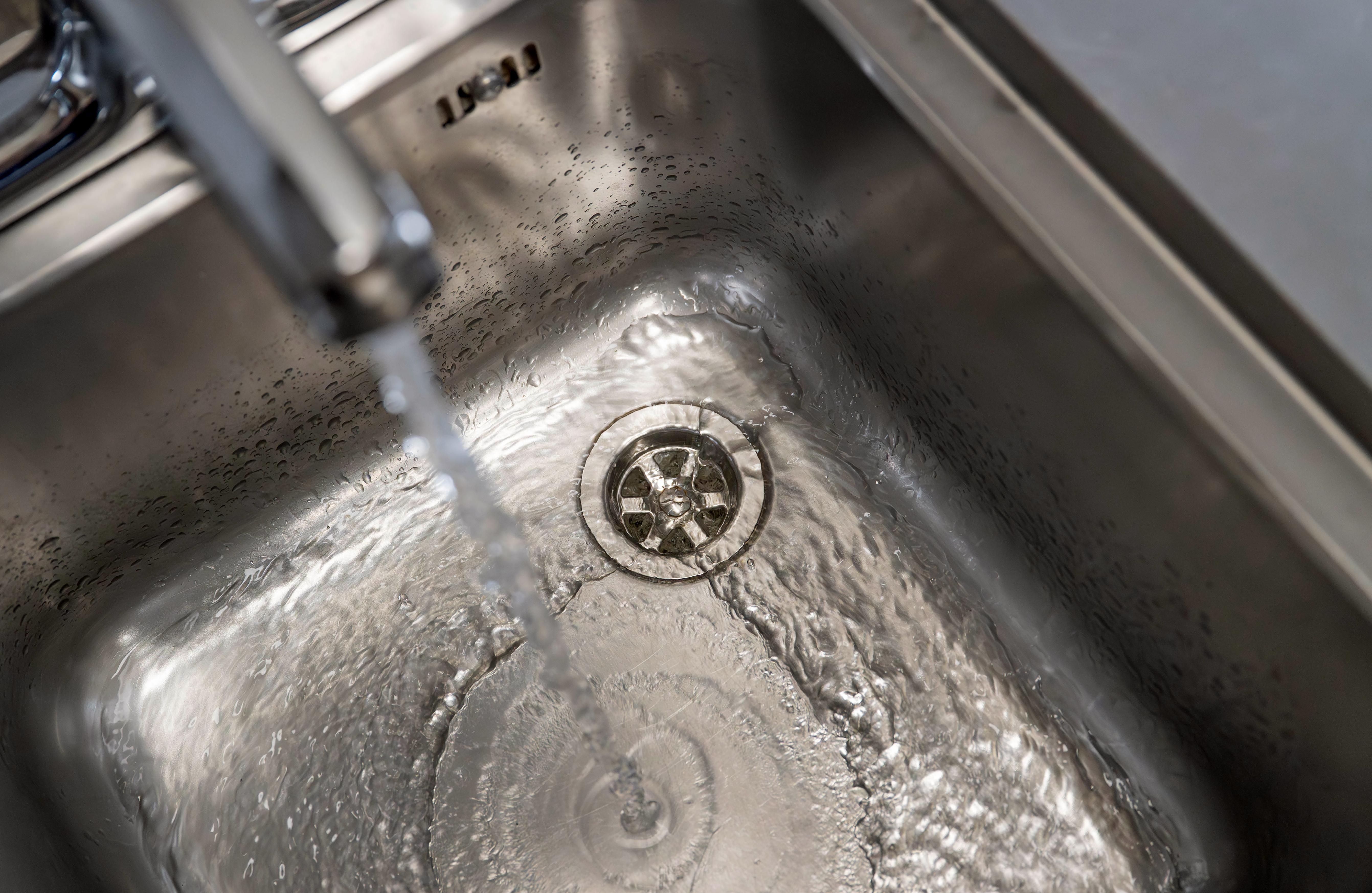 Water viewed from above flowing from tap down plug hole in commercial sink