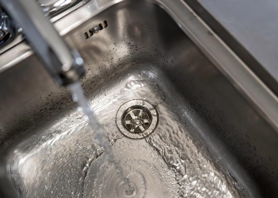 A running tap, with water flowing into an empty, metallic sink