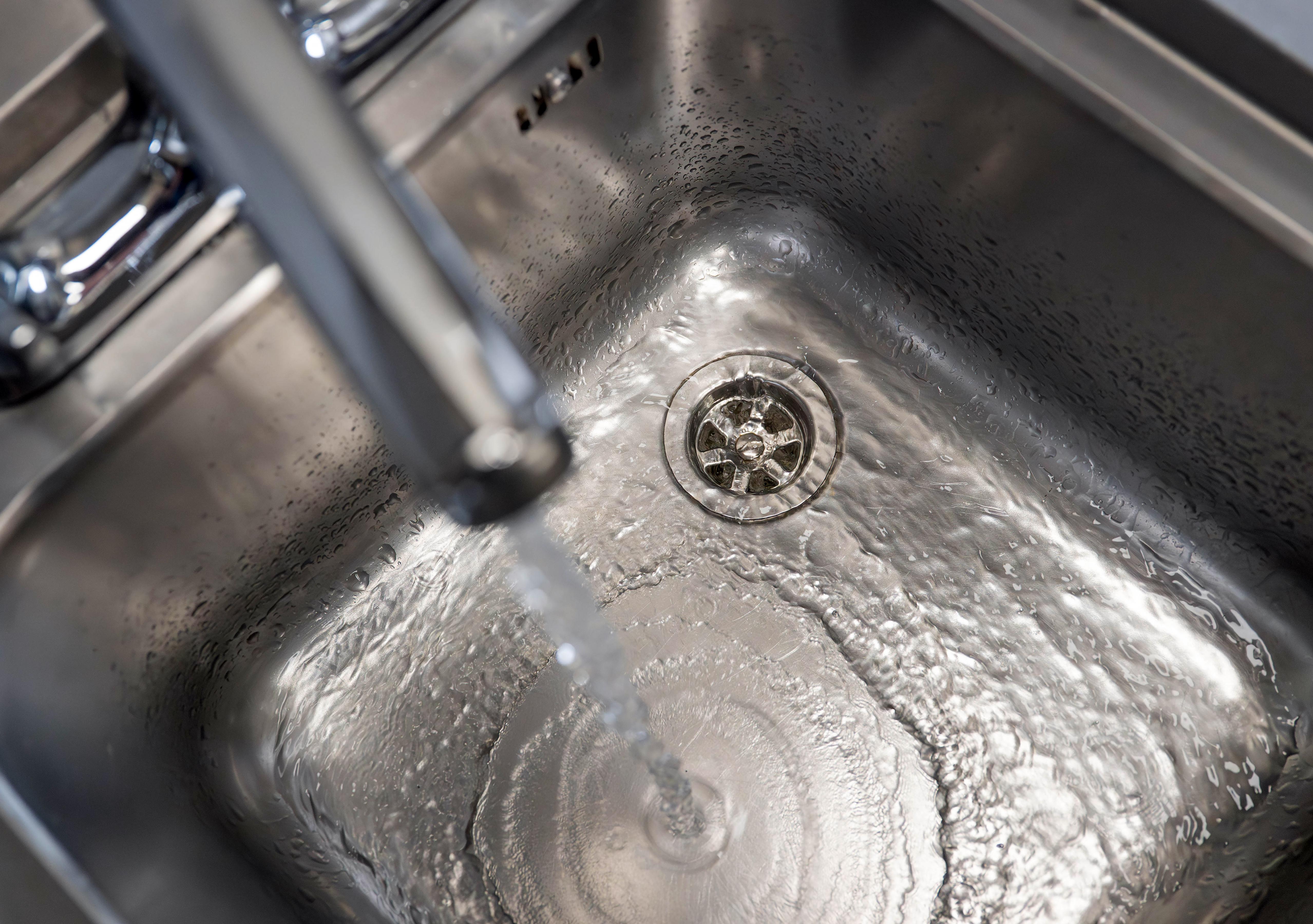 Water flowing from a tap viewed from above as it runs down a plug hole in a stainless steel sink