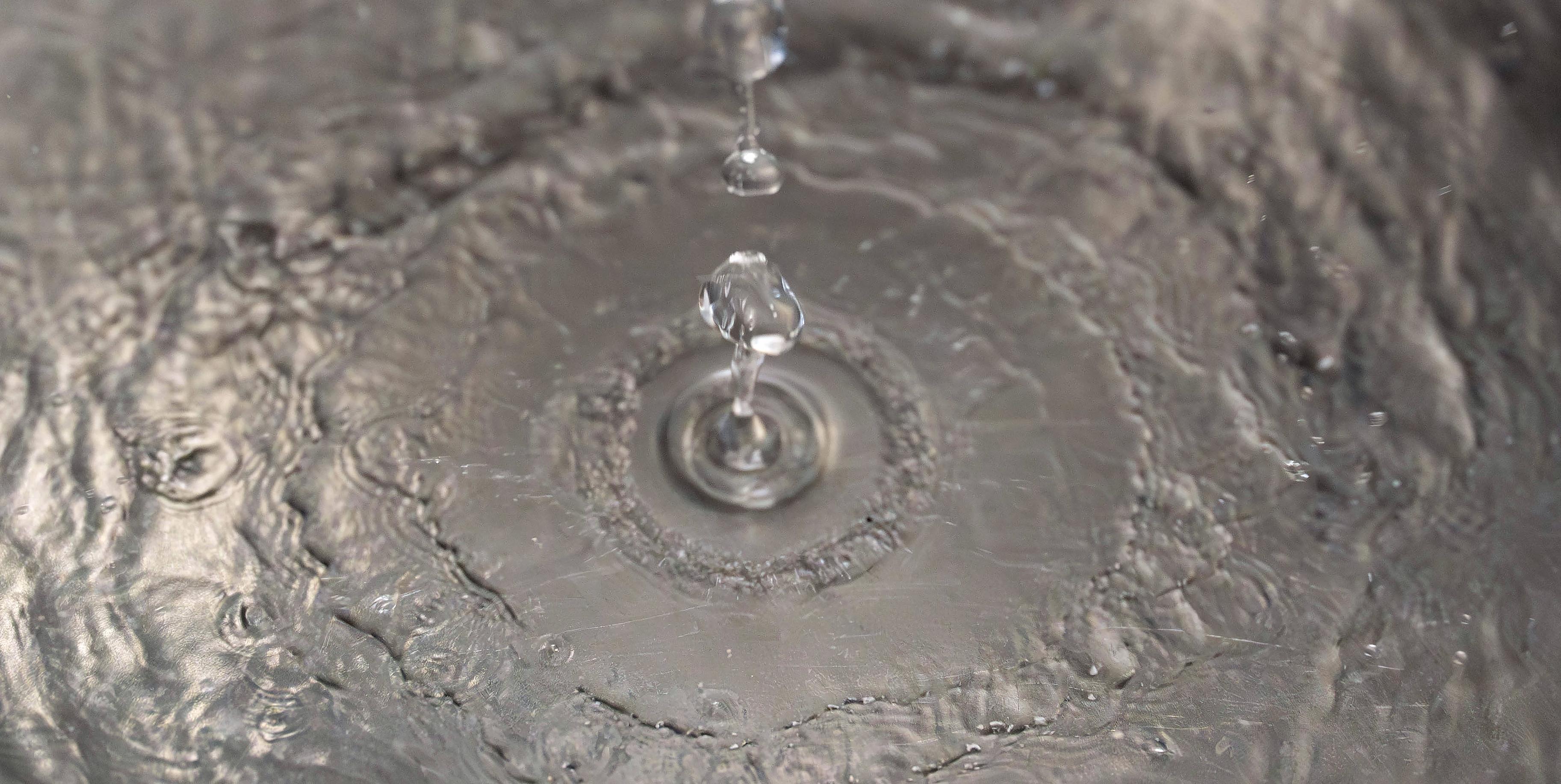 Close-up of water drop falling into steel sink