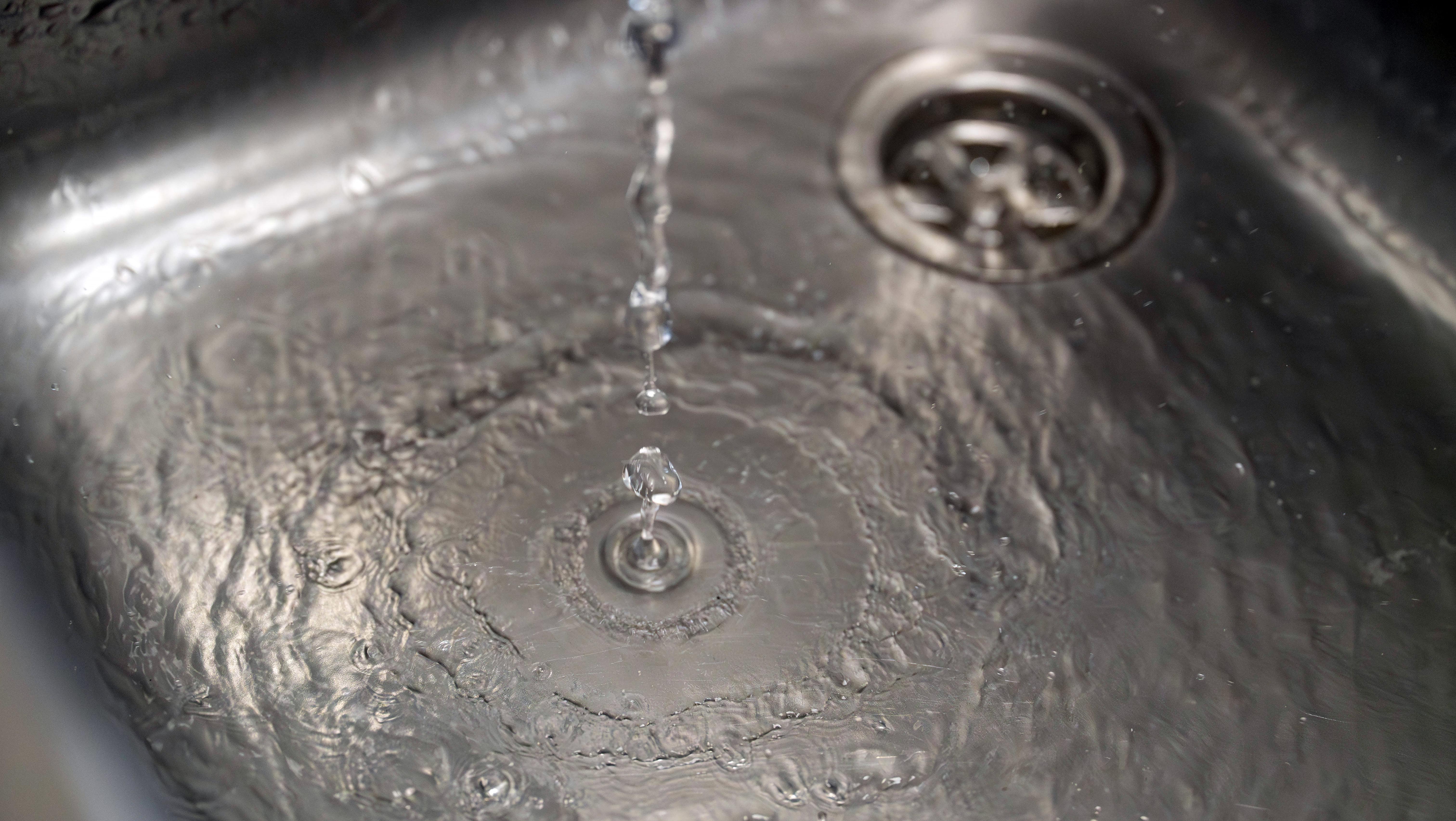 Close up of water flowing into a stainless steel sink and down the plug hole