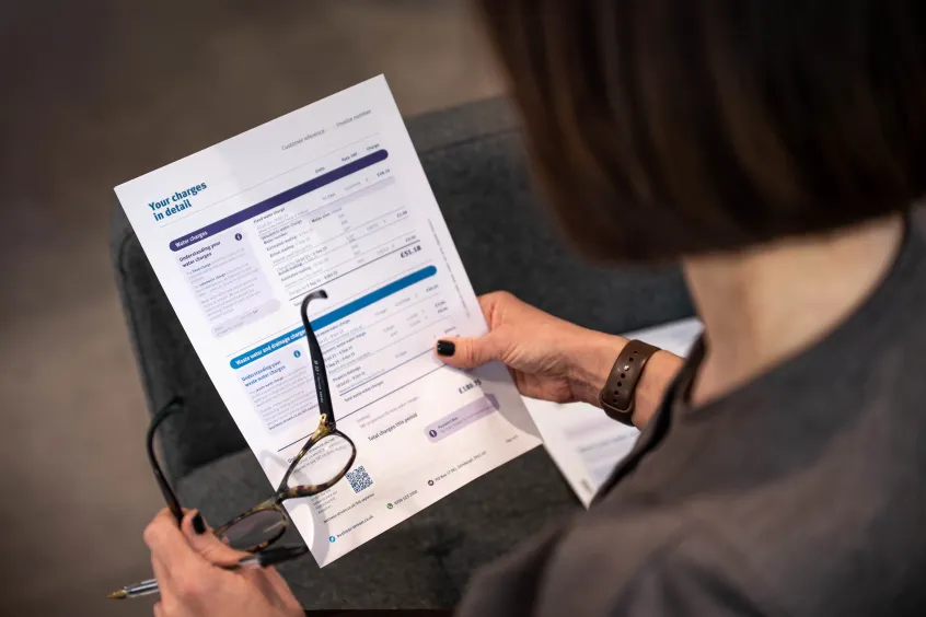 Over shoulder of woman looking at bill in her right hand, holding glasses in her left hand