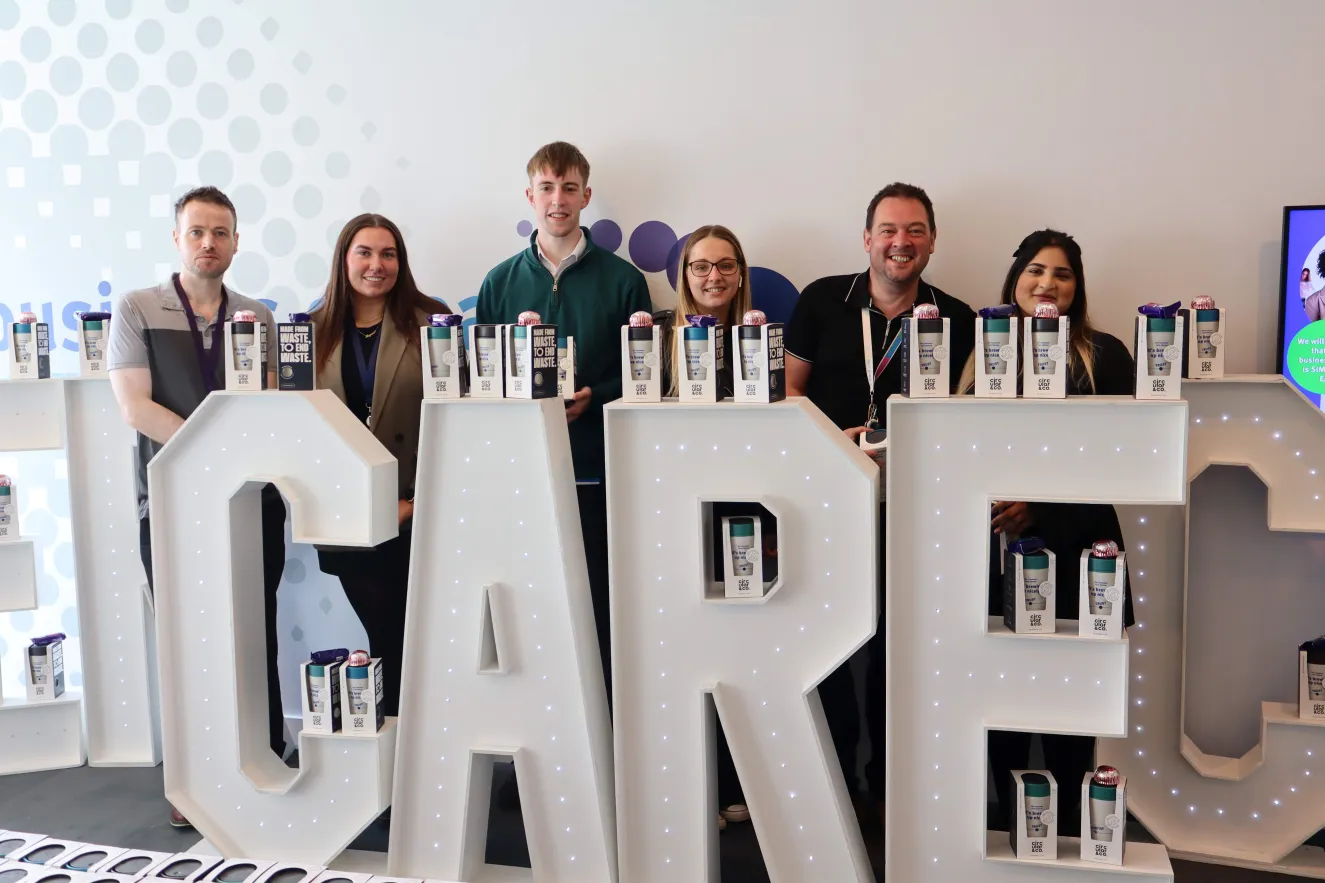 Six colleagues standing behind large floor-standing letters spelling out the world CARE