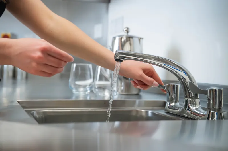 Close-up of woman's arms and hands as she operates tap at commercial sink
