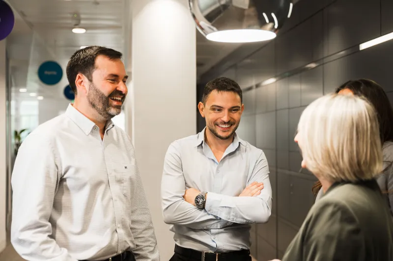 Woman and two men standing in Business Stream foyer chatting and smiling