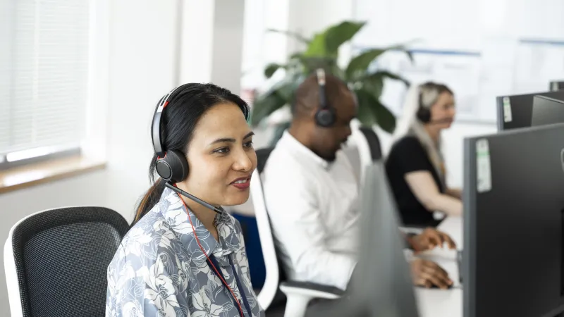 Smiling woman in Business Stream call centre with a man and another woman in the background