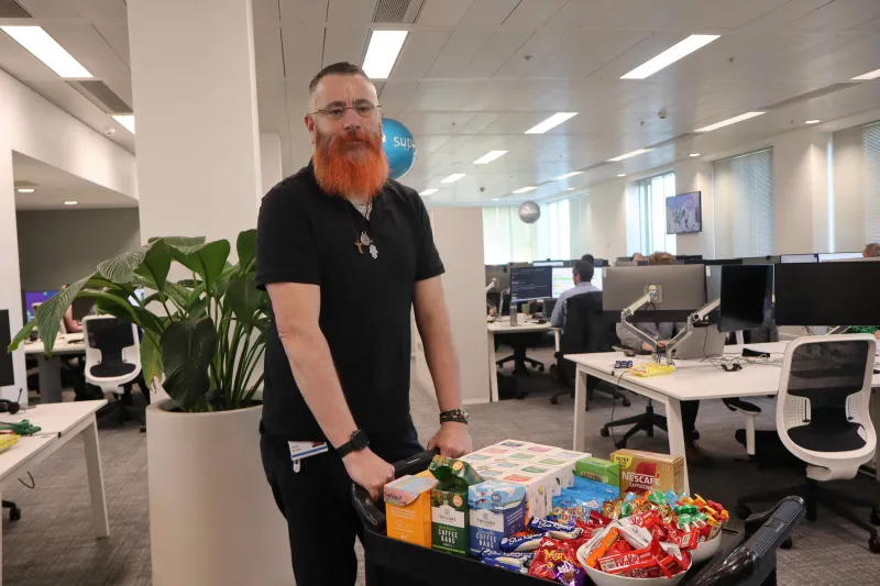 Man pushing trolley containing selection of teas and snacks in office setting