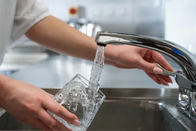 Close-up of water flowing from tap into a glass in a commercial kitchen with female hands visible